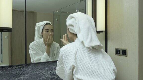 穿着白色浴衣的漂亮女人在浴室里使用护理霜在家里给脸部涂抹保湿霜的女人好的皮肤需要日常护理