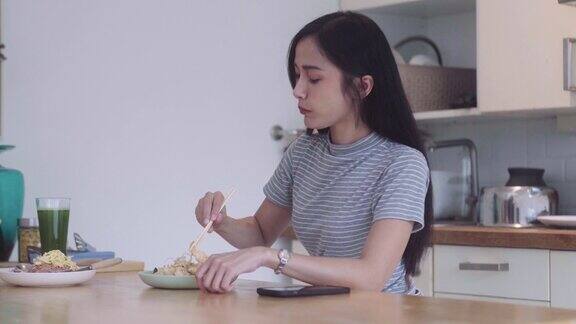 十几岁的亚洲女孩在家里的厨房里拿着筷子和泰式炒面吃午餐和饭