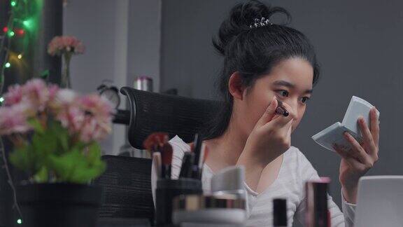 年轻的亚洲影响者女孩在视频中示范如何用美容化妆品化妆她在家里的客厅里用摄像机录制在线辅导课社交媒体和直播病毒概念