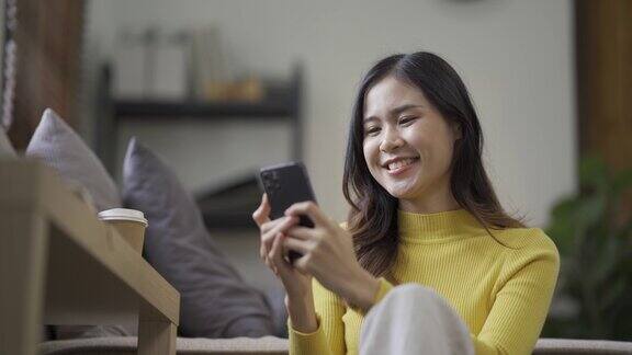 微笑的亚洲女性在家里用智能手机玩社交媒体、玩游戏、感觉快乐、发短信和网购在家生活的女人