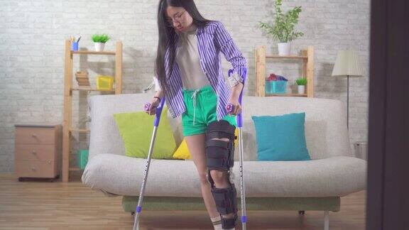 肖像年轻的亚洲女子受伤后膝盖弯曲矫正器使用拐杖从沙发上起来