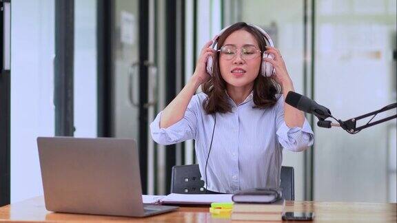 年轻漂亮的亚洲女电台主持人在广播演播室的办公桌前休息