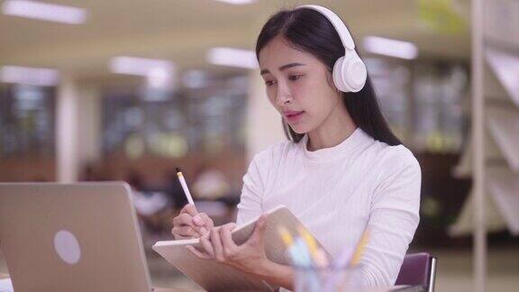 集中的亚洲青少年女学生坐在课桌和笔记本电脑上在线学习课程并在准备考试时写笔记