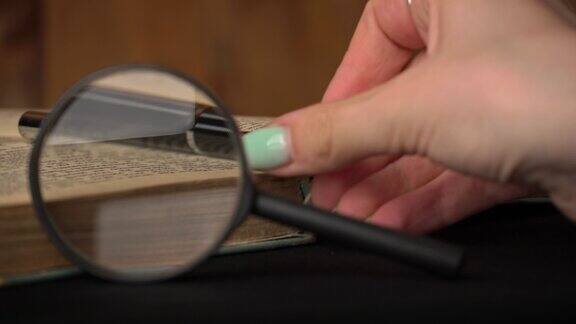 放大镜躺在一本旧书的背景上女孩拿着一支笔