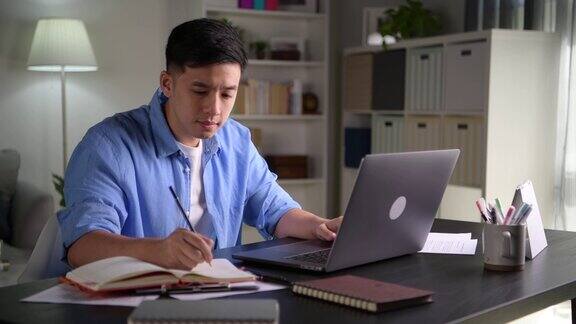年轻的亚洲商人坐在家里用笔记本电脑工作亚洲男子使用笔记本电脑上网学习信息