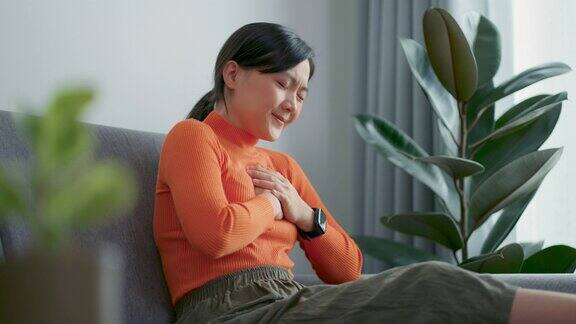 一位亚洲妇女坐在家里客厅的沙发上感到胸痛