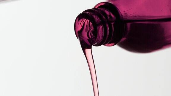 玫瑰油正从粉红色的瓶子倒在灰色的背景