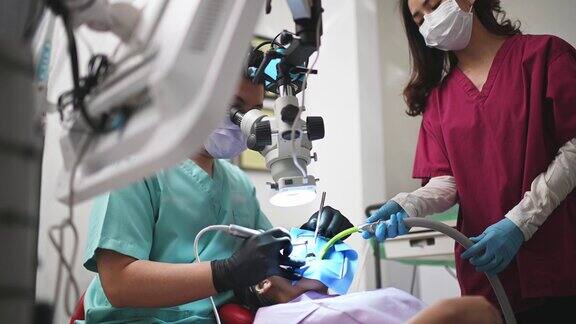 亚洲华裔男牙医在牙科诊所用显微镜观察病人的牙齿