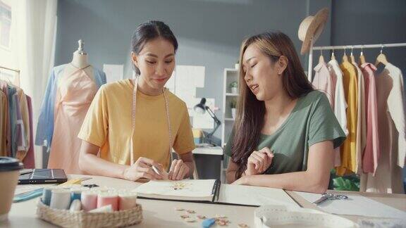 两位专业的亚洲开朗女士设计师团队合作与休闲会写生簿工作在店里讨论新时装系列的色彩分享想法女裁缝合伙人开始经营商店