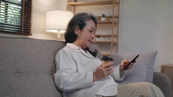 快乐的老年妇女晚上坐在家里的沙发上用电话进行网上交流面带微笑