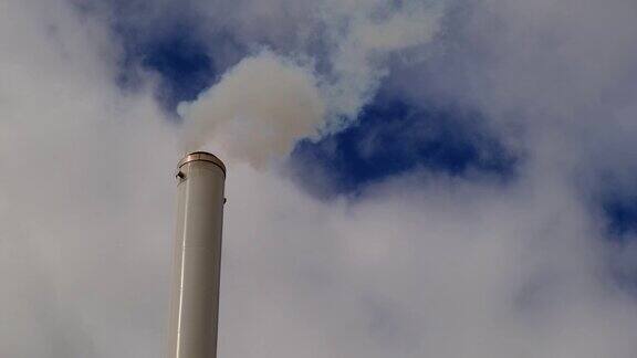 工厂的烟囱冒着烟映衬着蓝天白烟从烟囱里冒出来