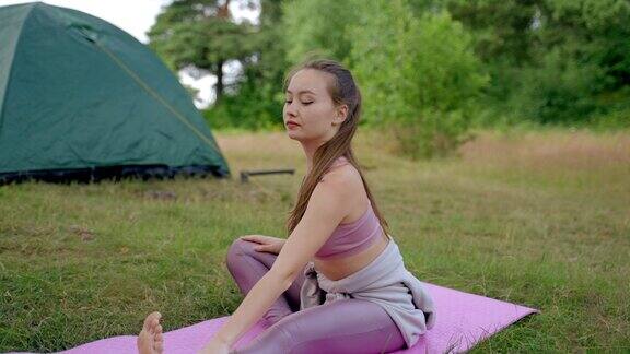 年轻的露营者在帐篷旁的粉红色垫子上舒展身体空气清新
