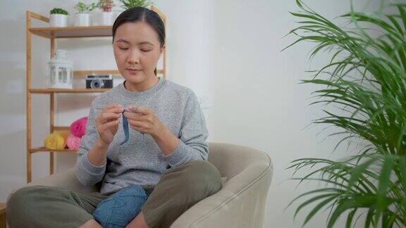 一名亚洲妇女坐在家里客厅的扶手椅上编织钩针
