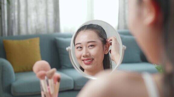 镜子里的倒影一个美丽的年轻亚洲女人微笑着整理她的头发准备在家里化妆