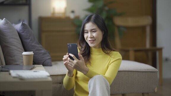 微笑的亚洲女性在家里用智能手机玩社交媒体、玩游戏、感觉快乐、发短信和网购在家生活的女人