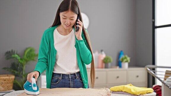 年轻的中国女子在洗衣房用智能手机熨衣服