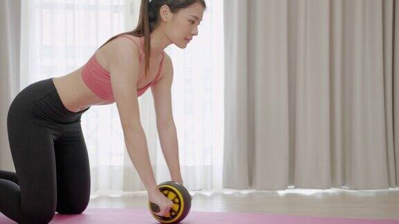 亚洲运动女性使用滚轮腹肌训练机锻炼腹肌和背部肌肉健身理念和健康