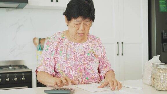 亚洲老年妇女在厨房整理支付账单和家庭财务通货膨胀和高生活成本