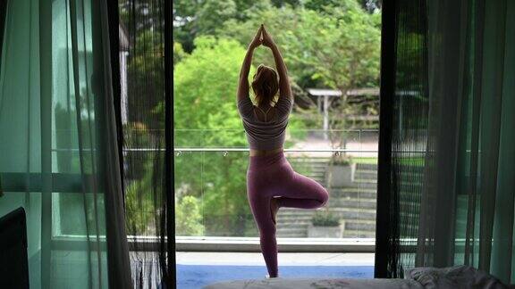 一个亚洲中国美丽的女人在她的房子在她的阳台练习瑜伽早上