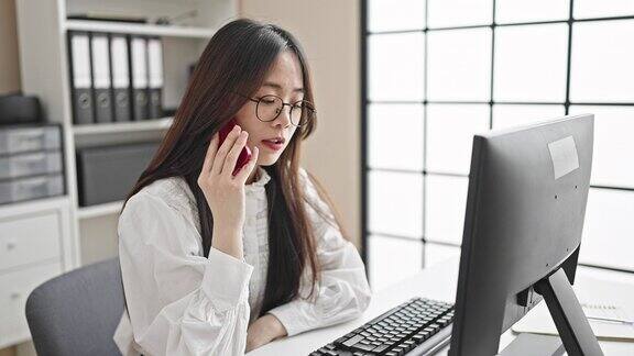 年轻的中国女商务工作者在办公室用电脑和智能手机聊天