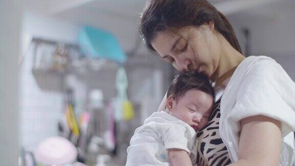 亚洲母亲拥抱睡着的婴儿儿子在厨房打盹