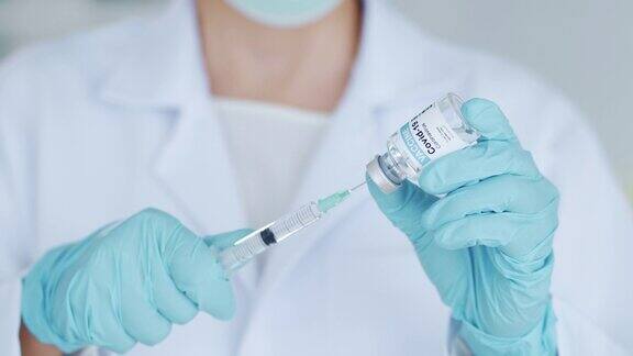 女医生或医师戴蓝色手套和医用口罩手持注射器和小瓶covid-19液体疫苗准备注射免疫和医疗