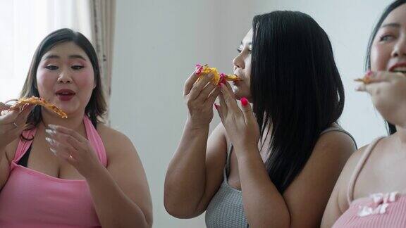 一群亚洲超重女性朋友喜欢在家里的客厅里一起吃披萨垃圾食品快餐不健康食品