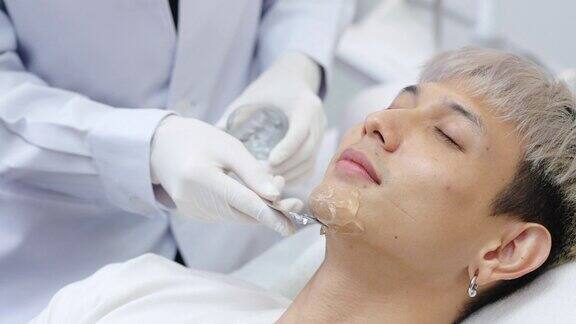 4K美容师在美容诊所进行激光脱毛前在亚洲男性脸上涂抹冷却凝胶