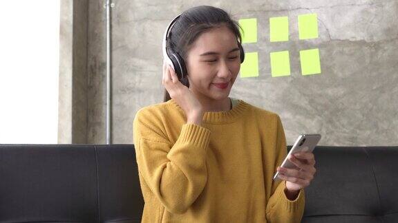 年轻的亚洲女性戴着耳机听着音乐在沙发上放松