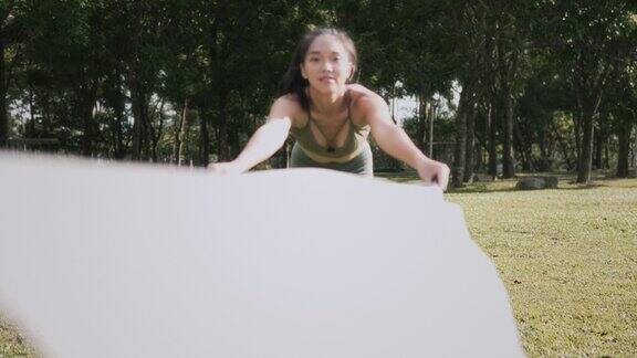 一名亚洲华裔妇女在草坪上铺开瑜伽垫准备锻炼