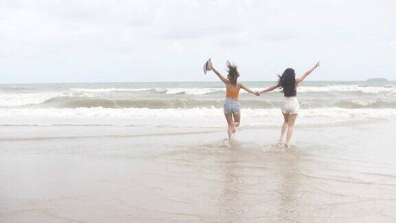 两个女人在沙滩上享受和奔跑手牵着手奔向大海