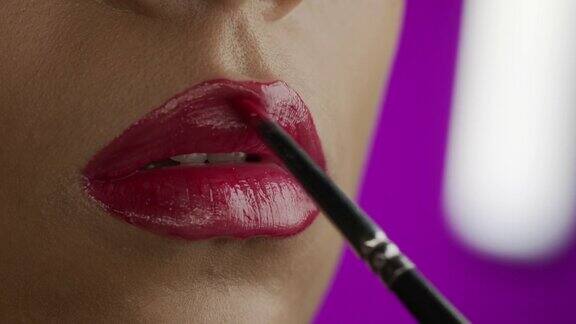特写镜头化妆师用化妆刷给女孩的嘴唇涂上红色的口红