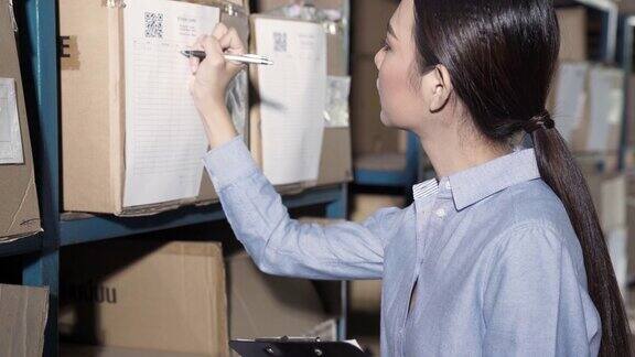 4K超高清手持式:亚洲女性仓库经理在仓库库存卡上使用条形码扫描仪进行库存清点