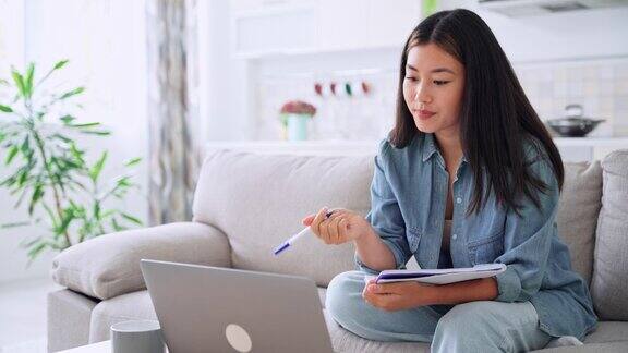亚洲青年妇女在笔记本电脑上看网络研讨会做笔记