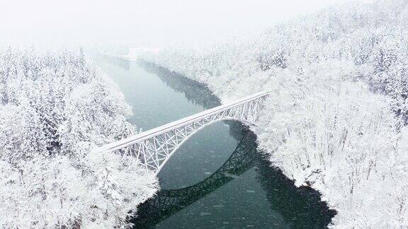4K鸟瞰图雪天横跨河流的山间铁路桥
