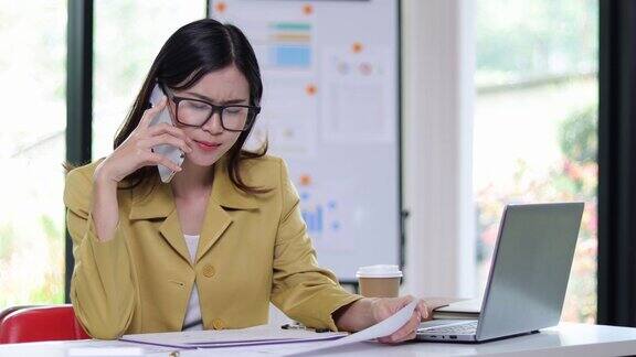一位女商人正在给客户打电话她在读办公室桌上的一些文件一个女人一边和别人打电话一边分析文件和阅读每月的工作计划