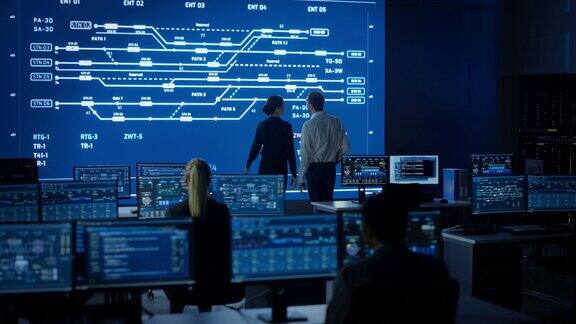 项目经理和计算机科学工程师在使用大屏幕显示基础设施信息图和数据时交谈有工作人员的电信控制监控室