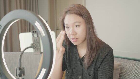 美丽的东南亚女性博主正在展示如何化妆和使用化妆品在摄像机前录制vlog视频直播在家在社交媒体和副业概念上的商业在线影响者