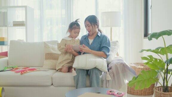 年轻的亚洲家庭妈妈和女儿在家里庆祝母亲节的时候在客厅的沙发上互相拥抱用心阅读手工制作的贺卡家庭幸福时刻