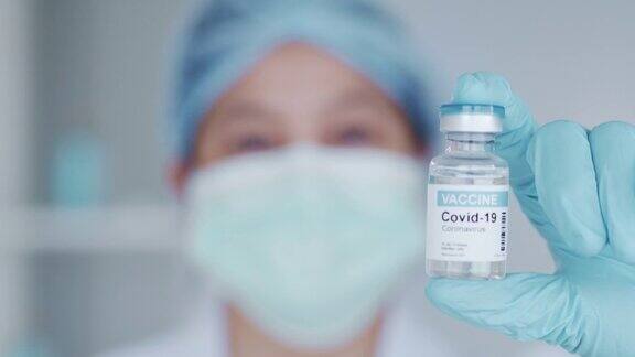 女医生或药剂师戴蓝色手套和医用口罩手持小瓶新型冠状病毒治疗液体疫苗用于预防2019年新型冠状病毒