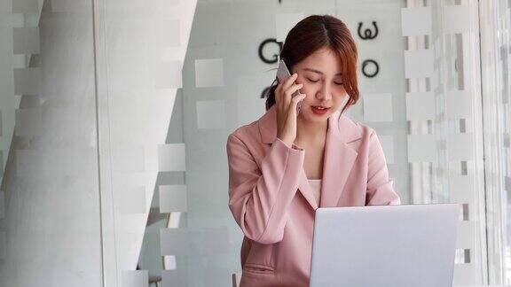 年轻的商业亚洲妇女专业的电话使用笔记本电脑坐在书桌前
