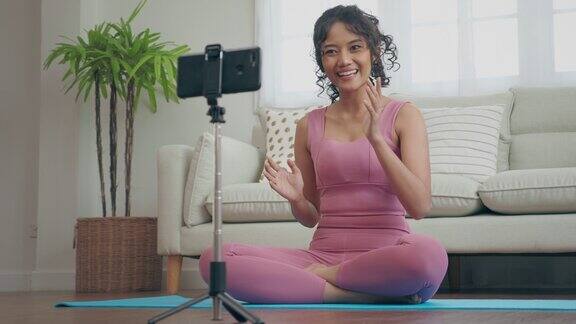 一名年轻女子正在家中通过智能手机直播瑜伽教学