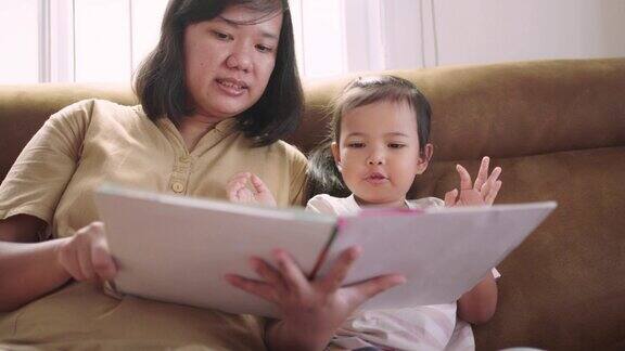 妈妈在教她的女儿在沙发上一起读书