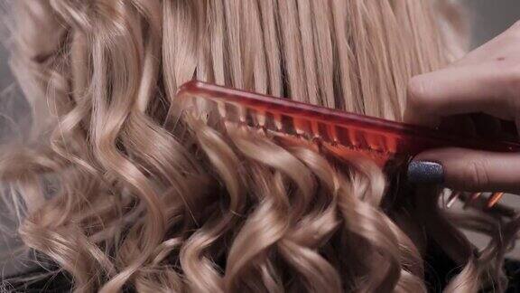一个女人的手用红色梳子梳理她卷曲的金发的特写