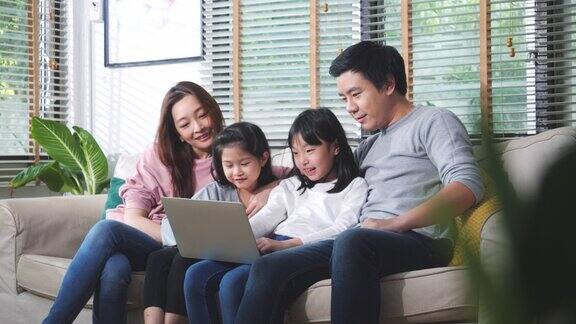 真实的亚洲家庭近距离观看电视节目在客厅的笔记本电脑在家里父亲、母亲和孩子在家隔离时在网上享受会议