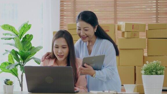 一名亚洲妇女和她的母亲在家用笔记本电脑和平板电脑在网上销售中小企业