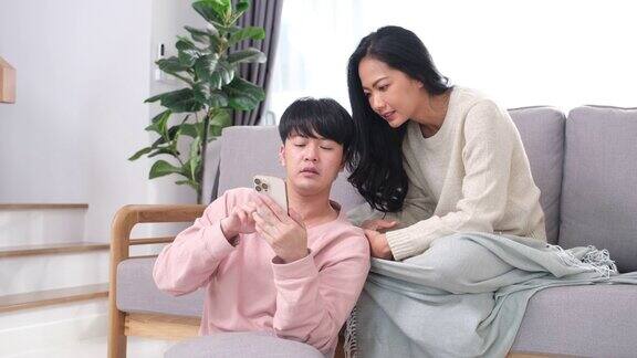 年轻的亚洲夫妇在家里客厅的沙发上用手机聊天