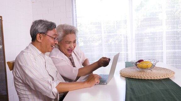 幸福的亚洲老年夫妇使用笔记本电脑在家里家庭放松和花时间在一起在家里退休人士和生活方式
