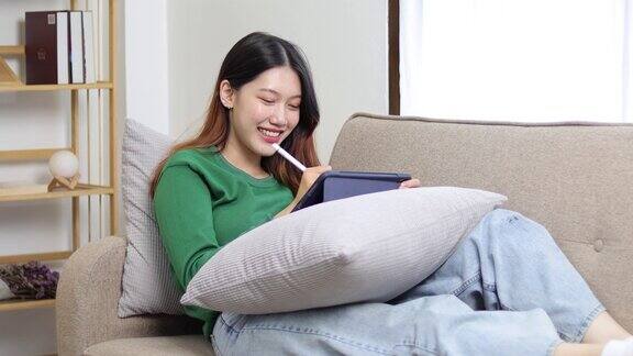 亚洲女性在客厅使用平板电脑同时在家里的沙发上放松