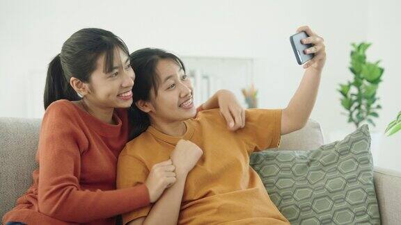亚洲两个女孩坐在家里的沙发上用智能手机自拍